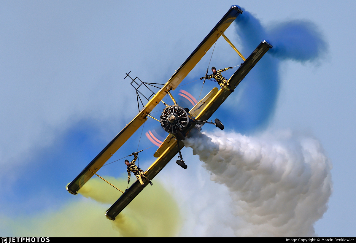 Wing‑walking biplane performing aerobatics with coloured smoke trails