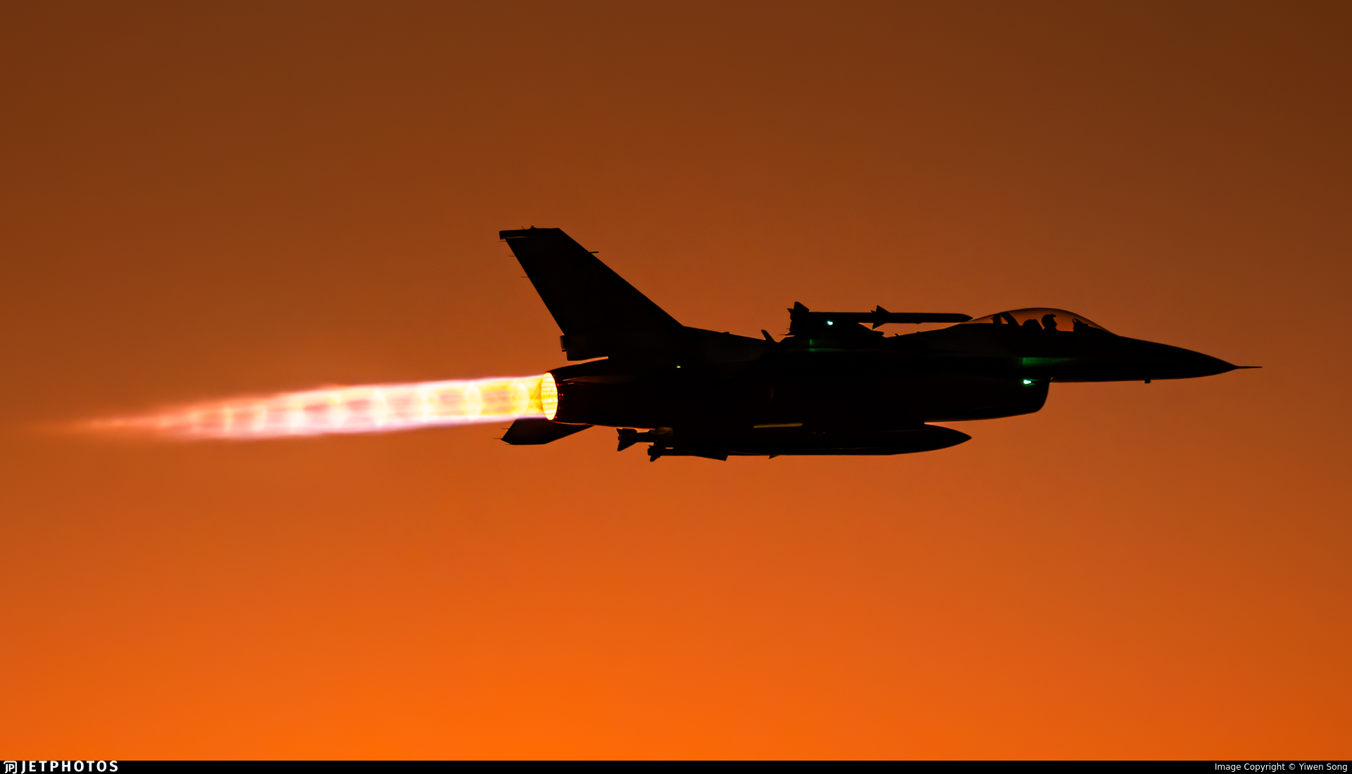 Silhouette of a fighter jet with afterburner glowing at sunset